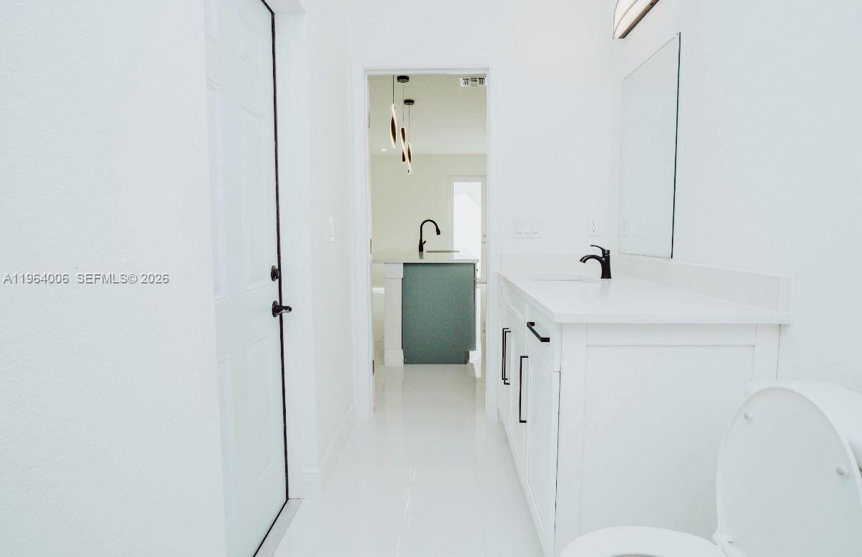 A bright bathroom features a white vanity, a mirror, and a doorway leading to a kitchen — 4405 E 7th, Lehigh Acres FL 33972, LEHIGH ACRES, FL