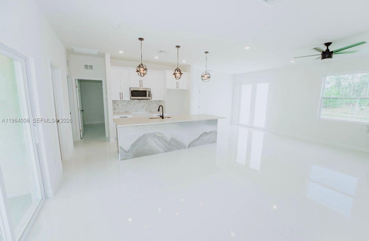 A modern kitchen features white cabinetry, a marble-patterned island, and glossy white tile floors — 4405 E 7th, Lehigh Acres FL 33972, LEHIGH ACRES, FL