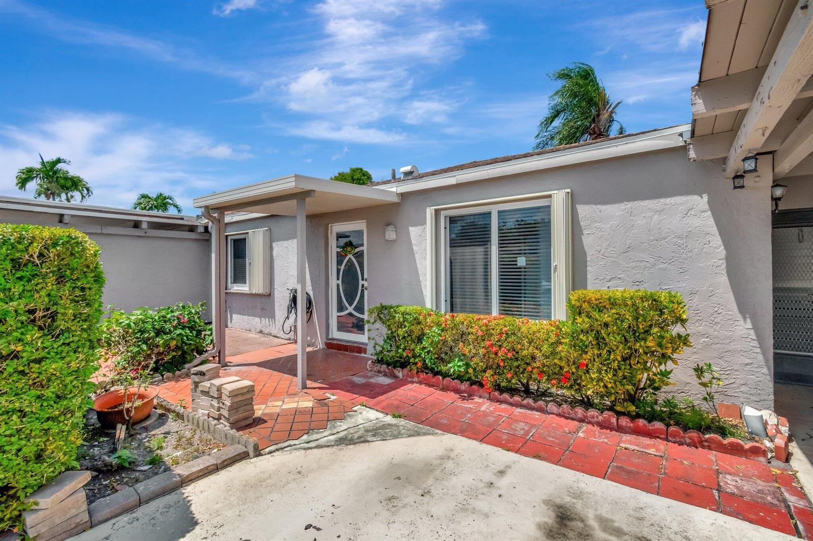 A gray house exterior features a red brick walkway, a covered entryway, and landscaped bushes — 14882 Wildflower Lane, Delray Beach FL 33446, DELRAY BEACH, FL