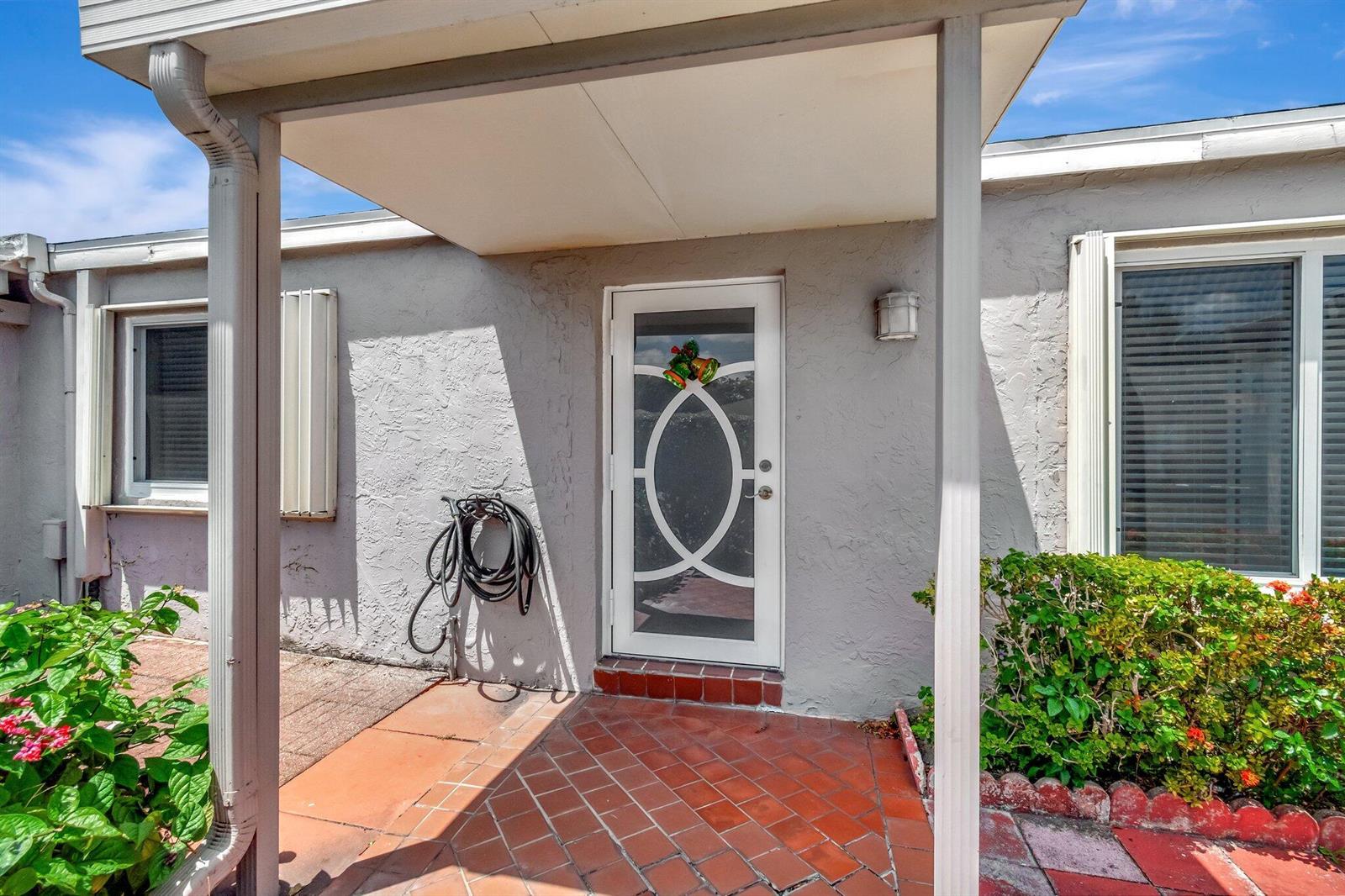 The exterior entrance features a white storm door, a tiled porch, and a covered walkway — 14882 Wildflower Lane, Delray Beach FL 33446, DELRAY BEACH, FL