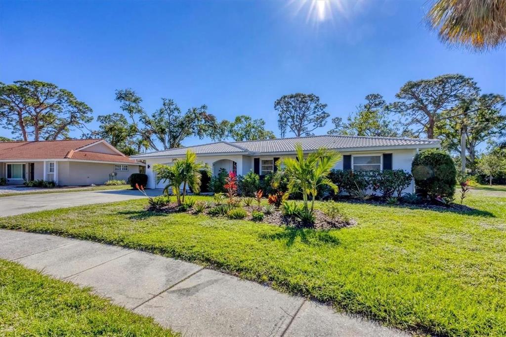 A single-story white house with a tiled roof sits behind a landscaped front yard — 2410 CASS STREET, SARASOTA, FL