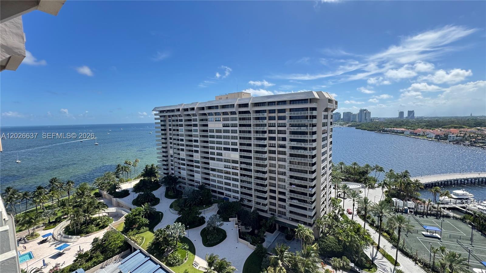 An aerial view shows a large residential building surrounded by tropical landscaping, a tennis court, and water — 2 Grove Isle Dr # B1706, Miami FL 33133, MIAMI, FL