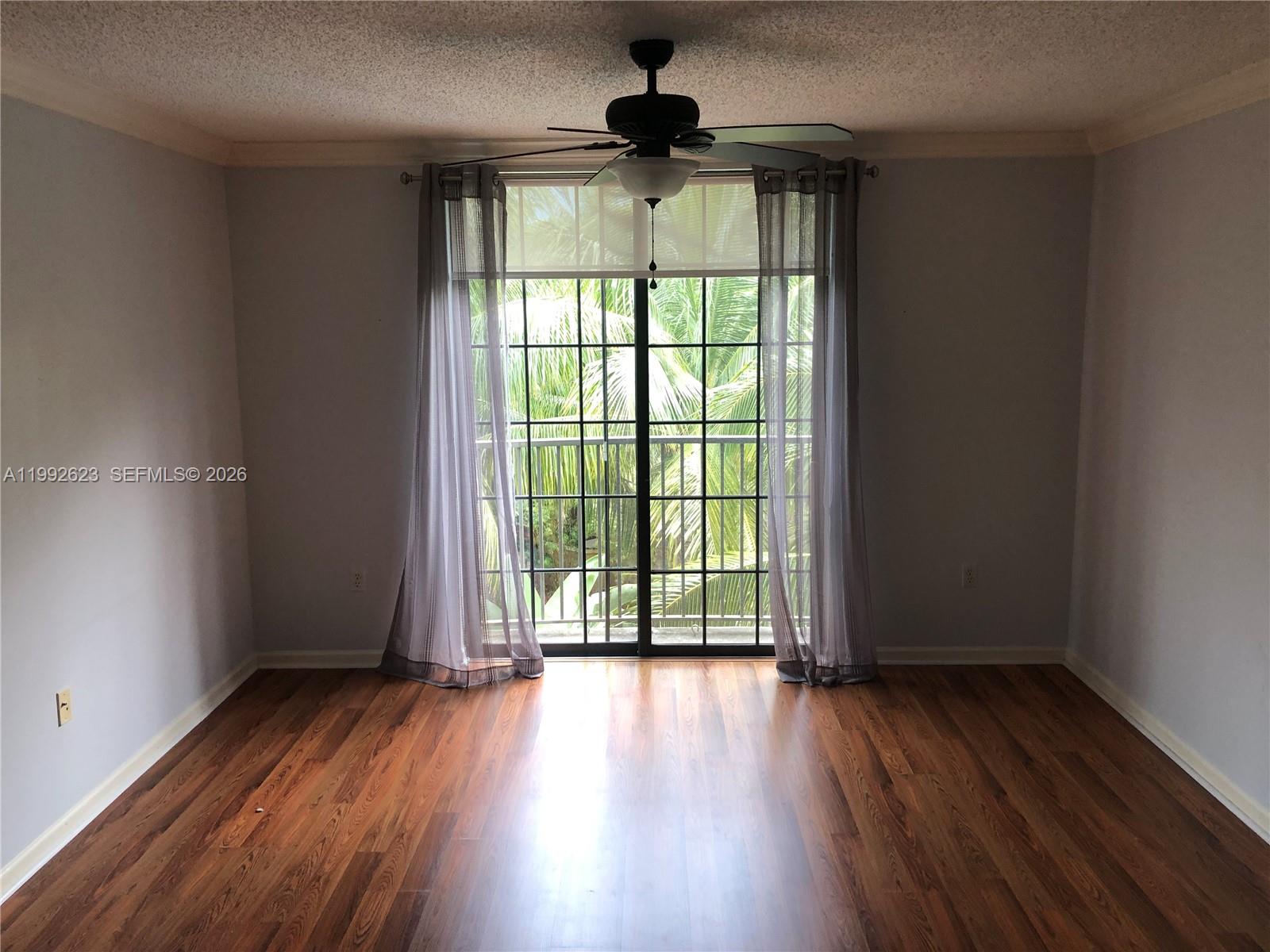 An empty room features wood-look flooring, a ceiling fan, and sliding glass doors with curtains — 1900 Van Buren St # 411B, Hollywood FL 33020, HOLLYWOOD, FL