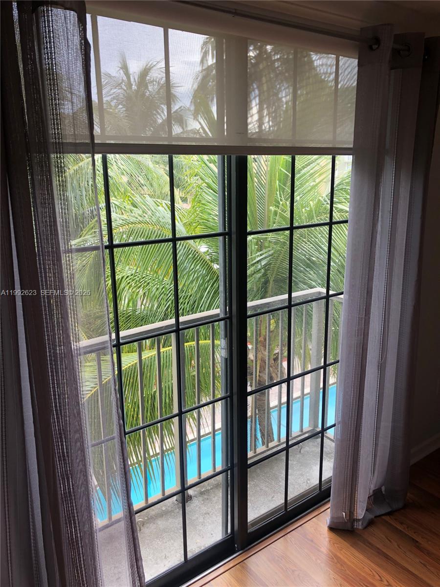 A window with sheer curtains overlooks a balcony, palm trees, and a swimming pool — 1900 Van Buren St # 411B, Hollywood FL 33020, HOLLYWOOD, FL