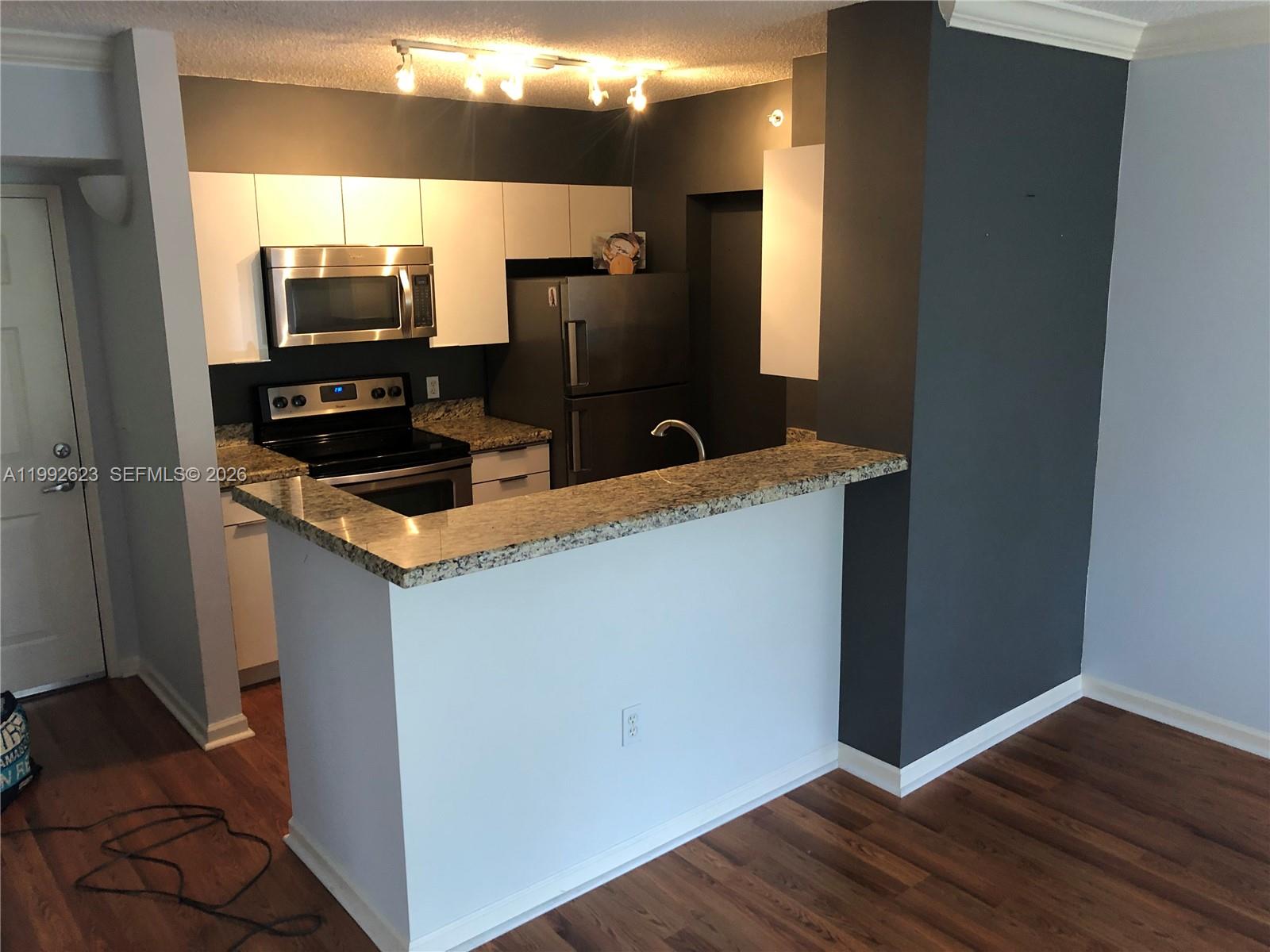 A kitchen features white cabinets, stainless steel appliances, granite countertops, and a dark accent wall — 1900 Van Buren St # 411B, Hollywood FL 33020, HOLLYWOOD, FL