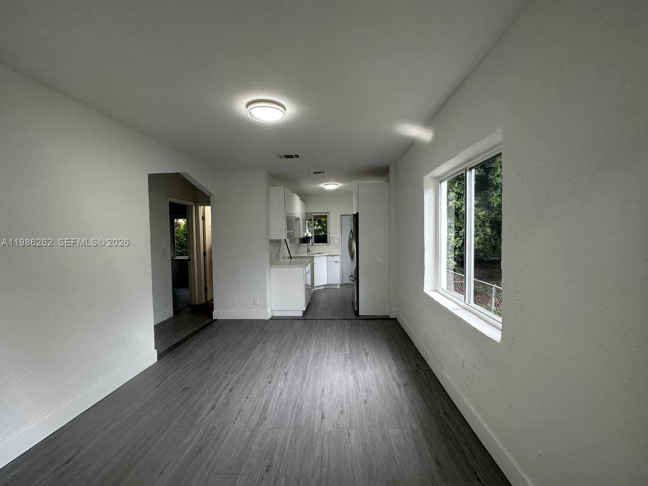 A bright kitchen with white cabinets and gray flooring opens into a living area — 1812 NW 64th St, Miami FL 33147, MIAMI, FL