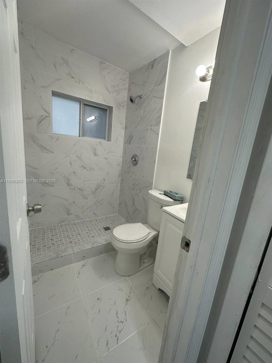 A small bathroom features white marble-look tile, a walk-in shower, and a pedestal vanity — 1812 NW 64th St, Miami FL 33147, MIAMI, FL