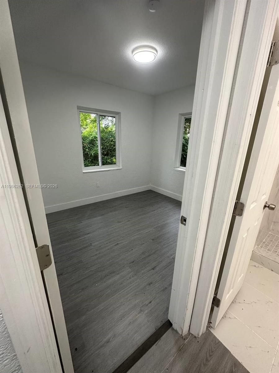 A small, empty room features white walls, gray wood-look flooring, and two windows — 1812 NW 64th St, Miami FL 33147, MIAMI, FL