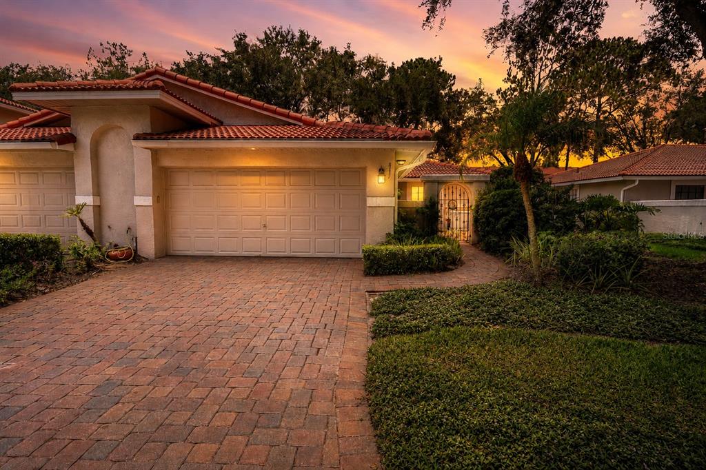 A single-story house with a tiled roof, brick driveway, and garage at sunset — 8237 BREEZE COVE LANE, ORLANDO, FL