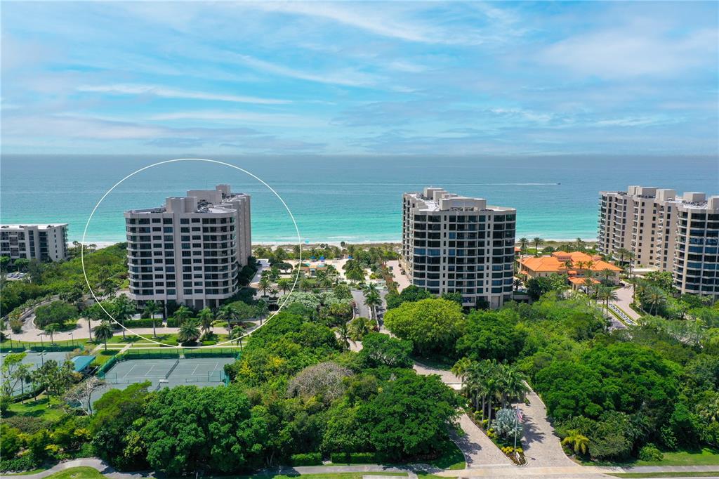 An aerial view shows a multi-story residential building circled on a lush, oceanfront property — 1211 GULF OF MEXICO DRIVE UNIT 302, LONGBOAT KEY, FL