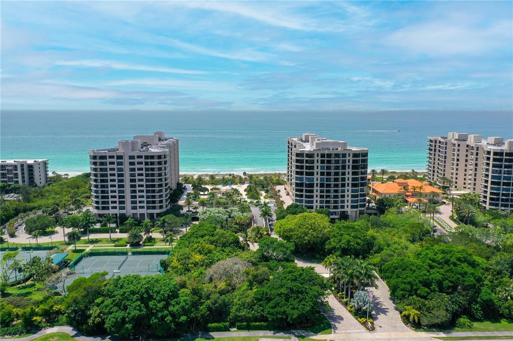 An aerial view shows three high-rise apartment buildings near a beach with tennis courts below — 1211 GULF OF MEXICO DRIVE UNIT 302, LONGBOAT KEY, FL
