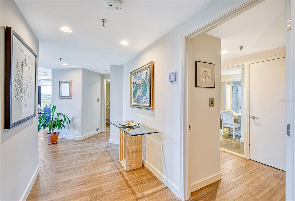A bright hallway with wood-look tile flooring, a glass console table, and framed wall art — 1211 GULF OF MEXICO DRIVE UNIT 302, LONGBOAT KEY, FL