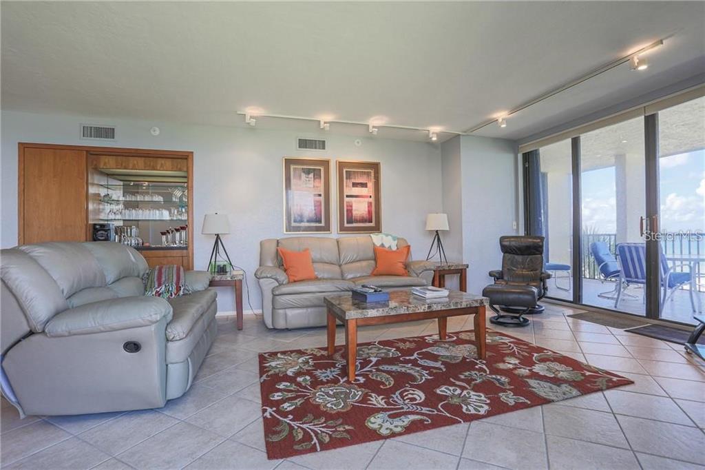A living room features light-colored leather sofas, a patterned rug, and a sliding glass balcony door — 1925 GULF OF MEXICO DRIVE UNIT 309, LONGBOAT KEY, FL