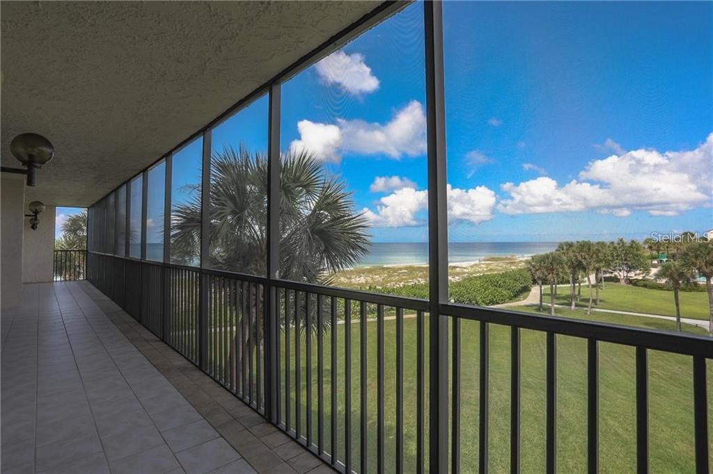 A screened-in balcony overlooks a grassy lawn, palm trees, and the ocean under a blue sky — 1925 GULF OF MEXICO DRIVE UNIT 309, LONGBOAT KEY, FL