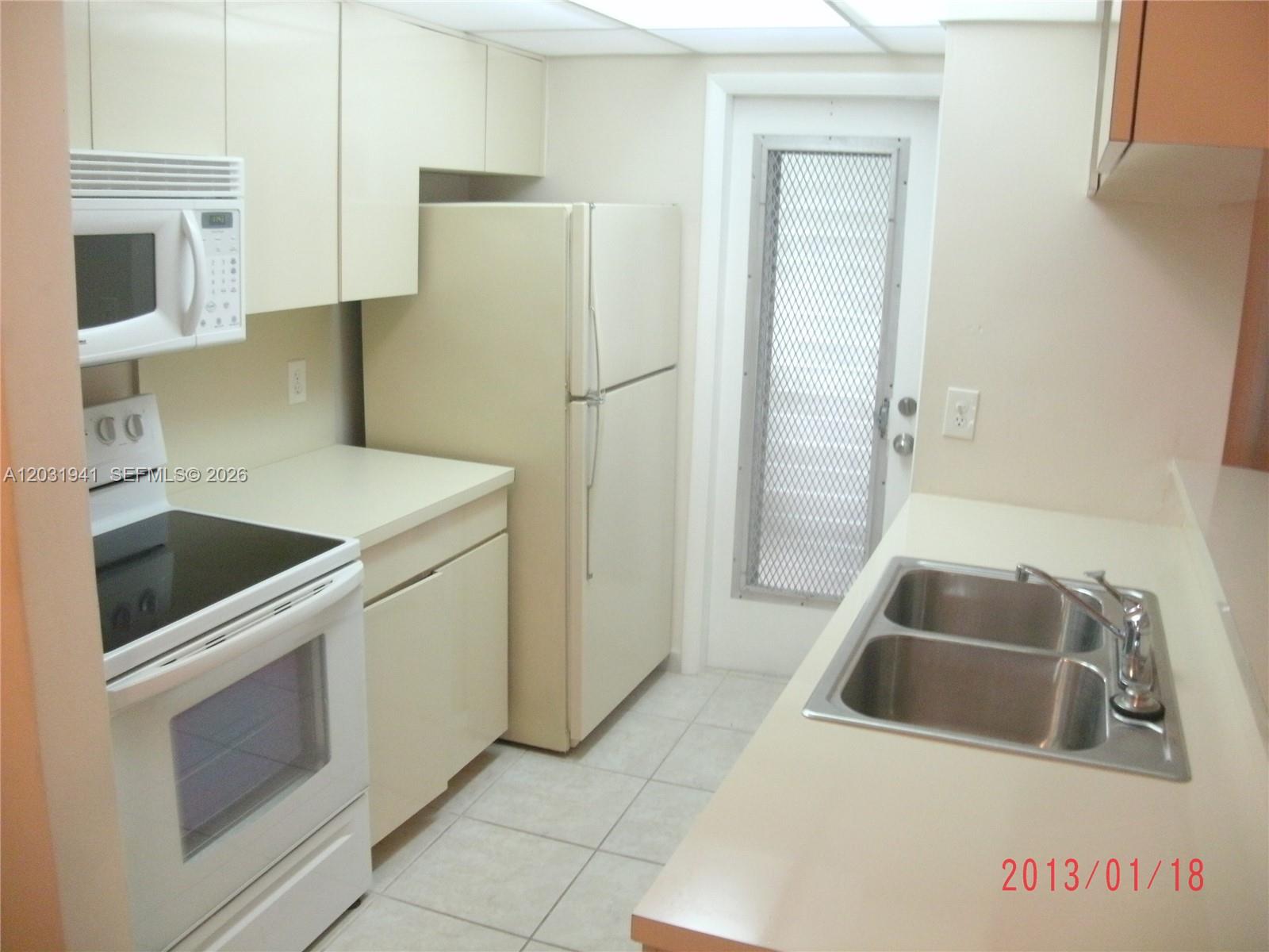 A kitchen features white appliances, light-colored cabinetry, a double sink, and a screen door — 2700 NE 135th St # 30, North Miami FL 33181, NORTH MIAMI, FL