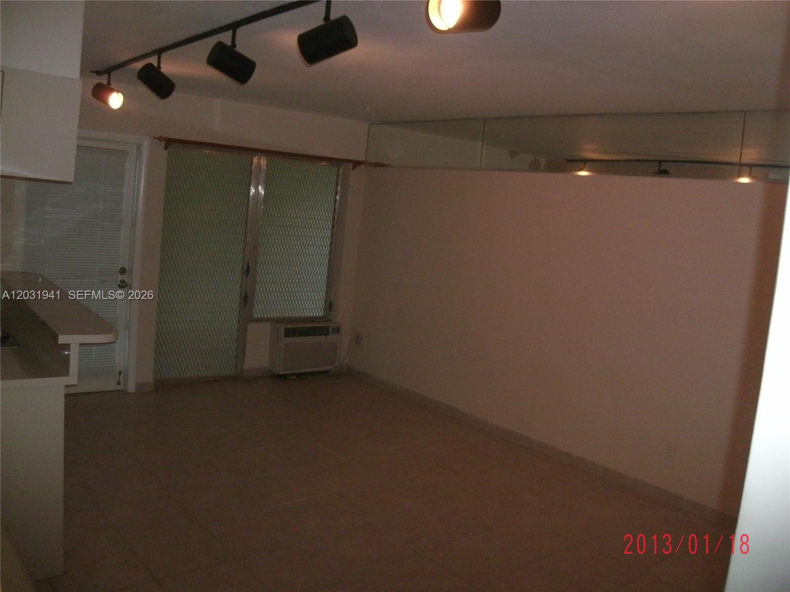 An empty room features tile flooring, track lighting, a sliding glass door, and mirrored walls — 2700 NE 135th St # 30, North Miami FL 33181, NORTH MIAMI, FL