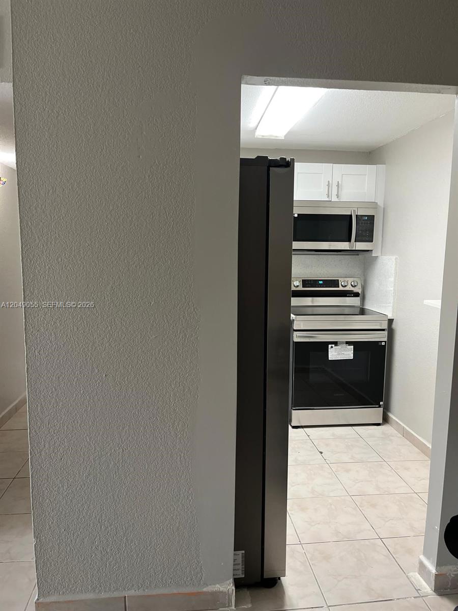 A kitchen features stainless steel appliances, white cabinets, and light-colored tile flooring — 666 W 81st St # 318, Hialeah FL 33014, HIALEAH, FL