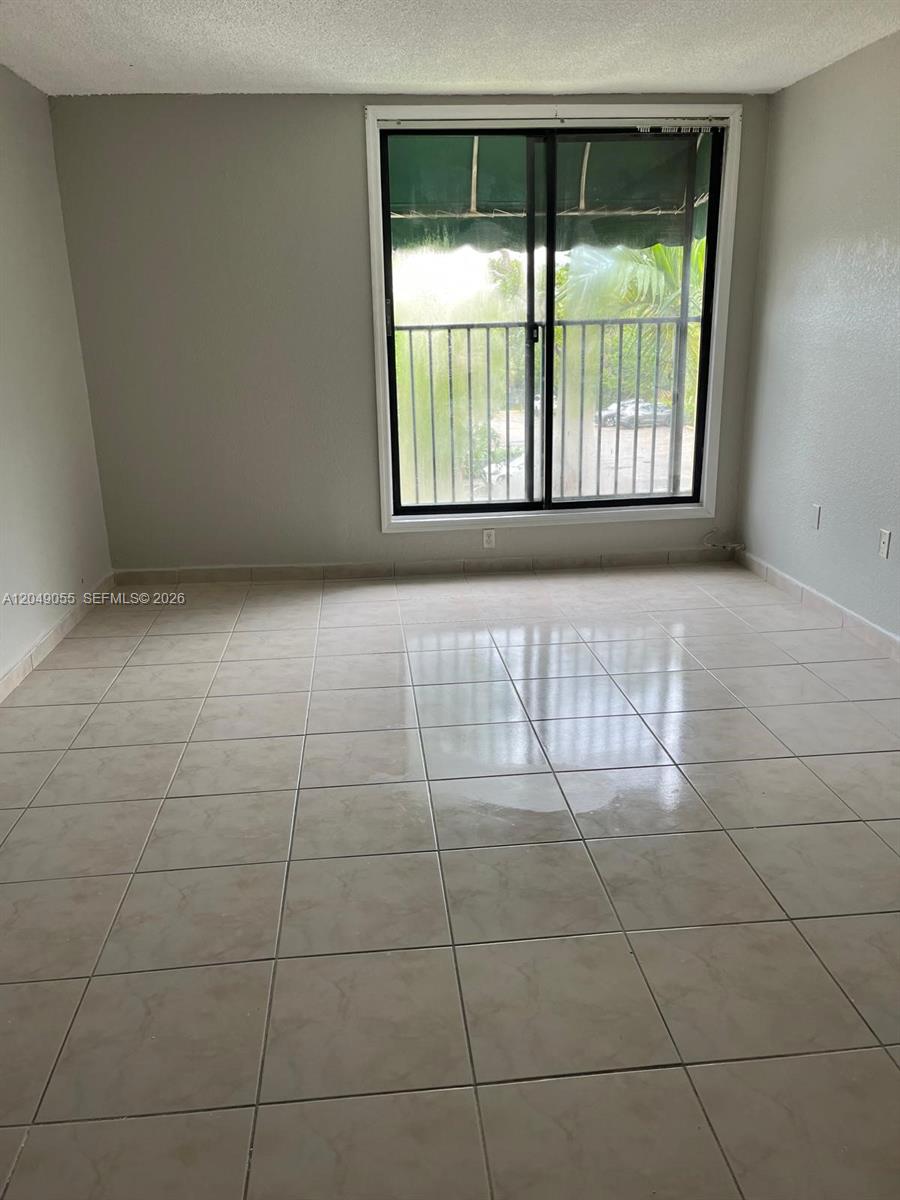 An empty room features light-colored tile flooring, gray walls, and a sliding glass balcony door — 666 W 81st St # 318, Hialeah FL 33014, HIALEAH, FL