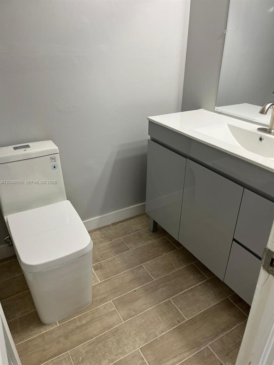 A modern bathroom features a white toilet, a gray vanity with a sink, and wood-look tile — 666 W 81st St # 318, Hialeah FL 33014, HIALEAH, FL