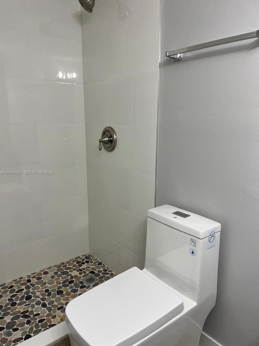 A bathroom features a walk-in shower with pebble flooring and a white toilet — 666 W 81st St # 318, Hialeah FL 33014, HIALEAH, FL