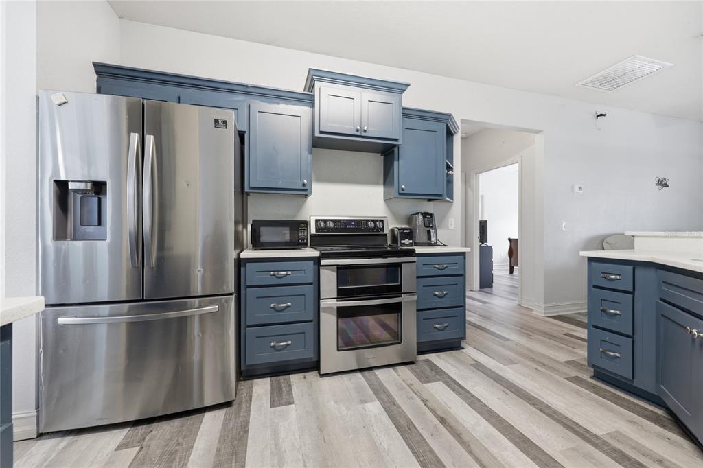 A kitchen features blue cabinets, stainless steel appliances, and wood-look plank flooring — 2750 NW 174TH STREET, TRENTON, FL