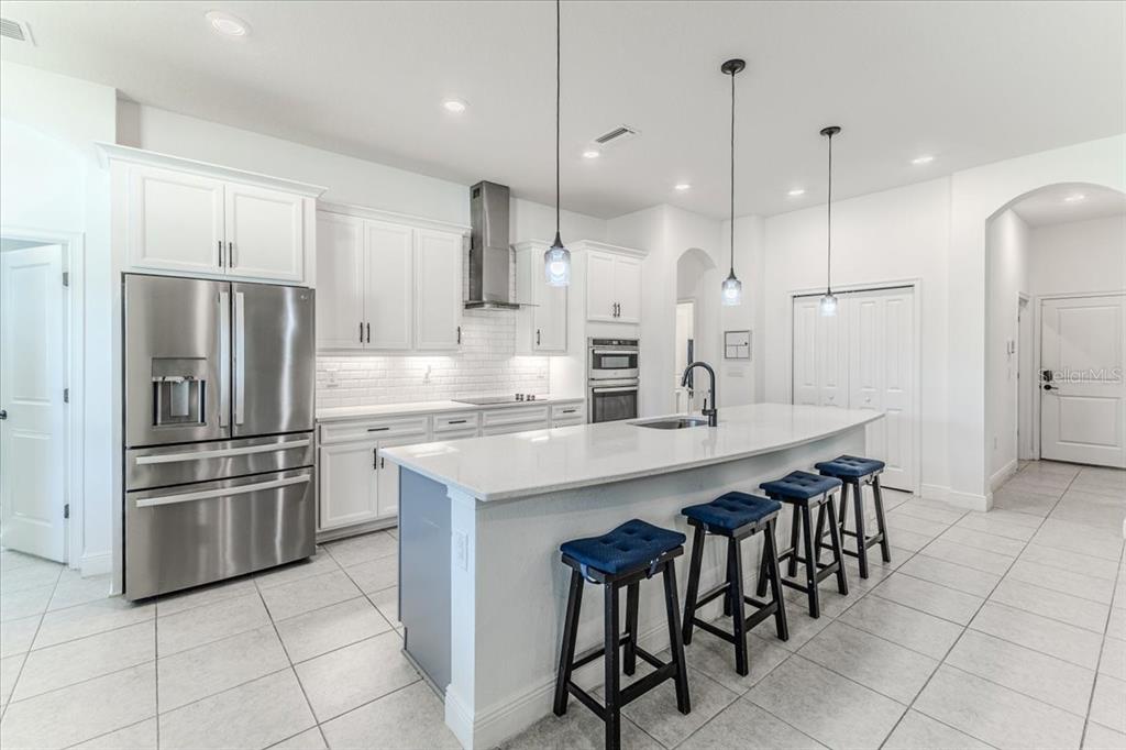 A modern kitchen features white cabinetry, stainless steel appliances, a large island, and tile flooring — 1252 KELSA ANNE DRIVE, SPRING HILL, FL