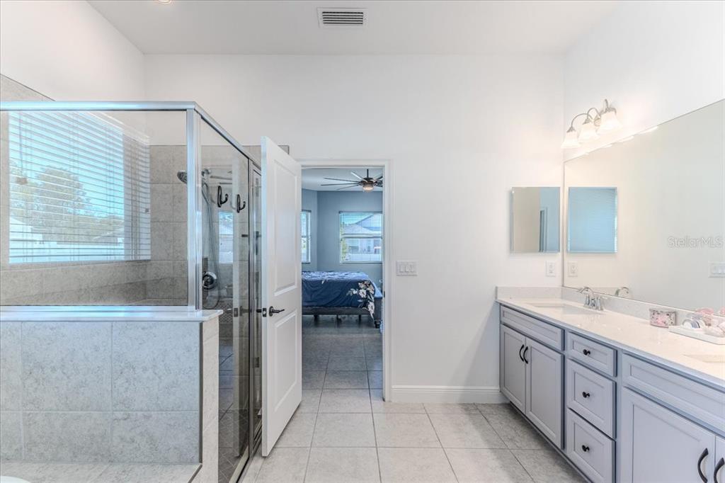 A bathroom with a glass-enclosed shower, gray vanity, and a doorway leading to a bedroom — 1252 KELSA ANNE DRIVE, SPRING HILL, FL
