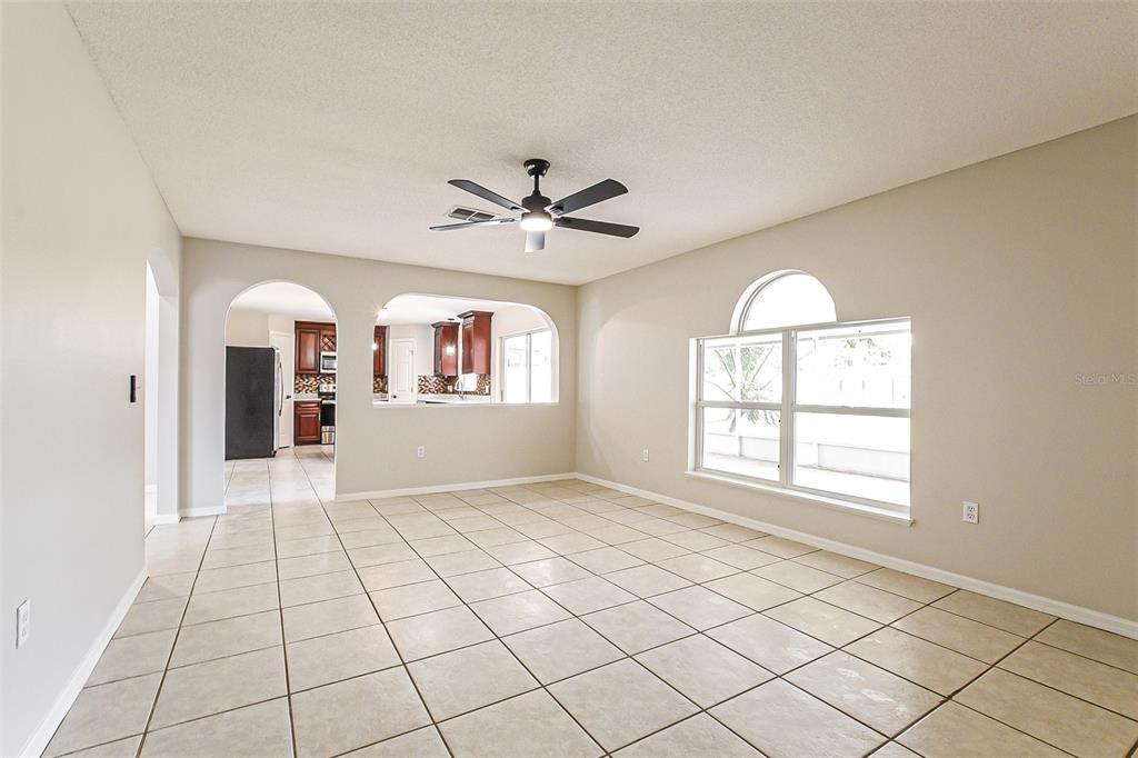 A tiled living room features a ceiling fan and an arched opening to the kitchen — 10019 DEAN CHASE BOULEVARD, ORLANDO, FL