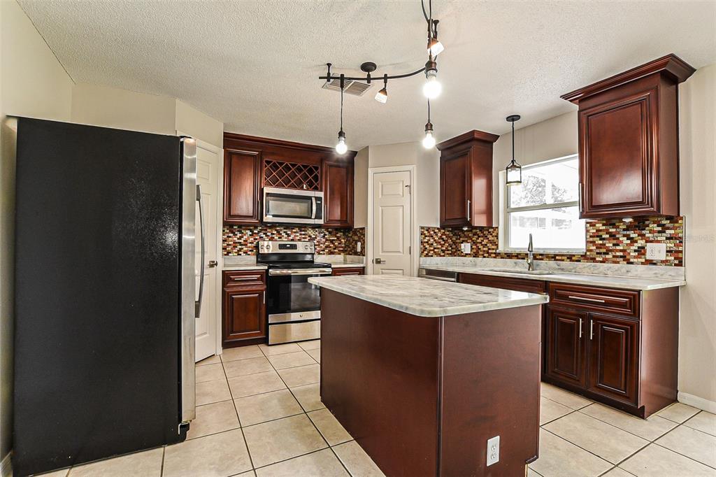 A kitchen features dark wood cabinets, a center island, stainless steel appliances, and tile flooring — 10019 DEAN CHASE BOULEVARD, ORLANDO, FL