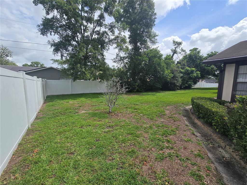 A grassy backyard features a small tree, a white vinyl fence, and a house exterior — 4632 BLOSSOM BOULEVARD UNIT 4632, ZEPHYRHILLS, FL