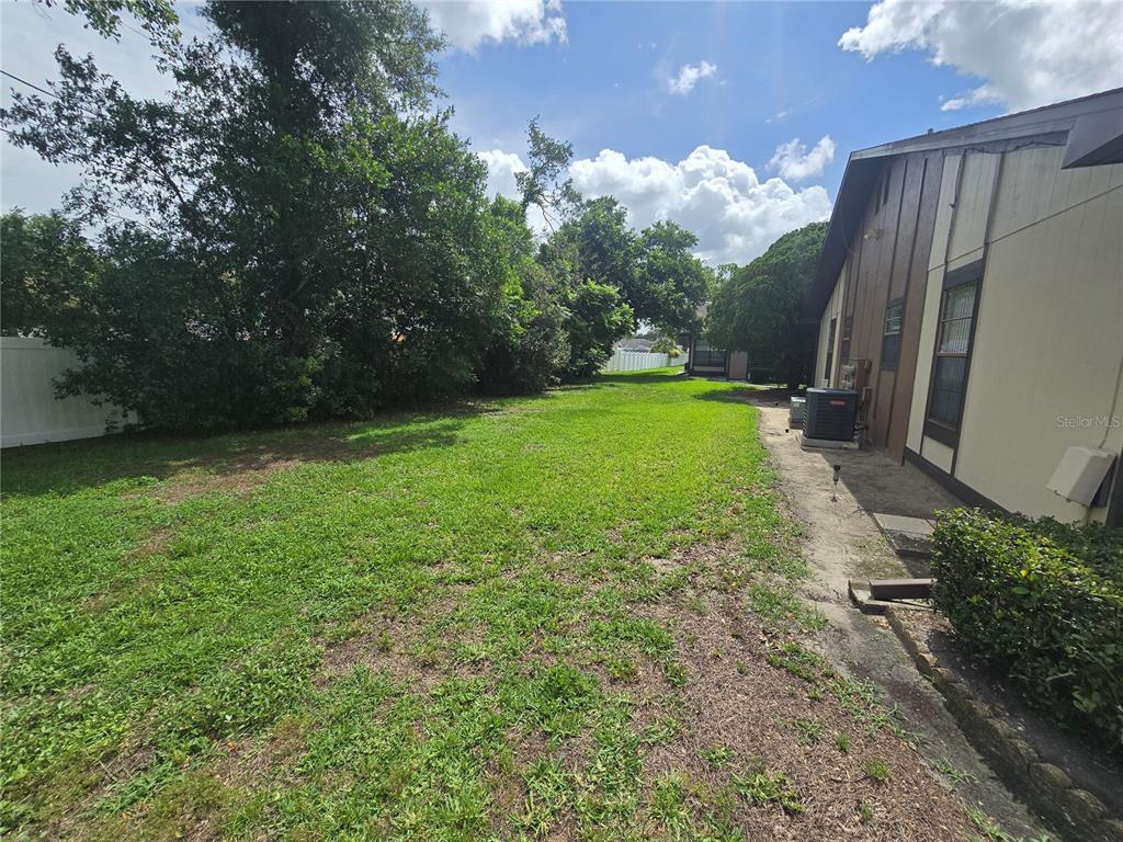 A grassy backyard extends alongside the side of a house with a concrete walkway — 4632 BLOSSOM BOULEVARD UNIT 4632, ZEPHYRHILLS, FL