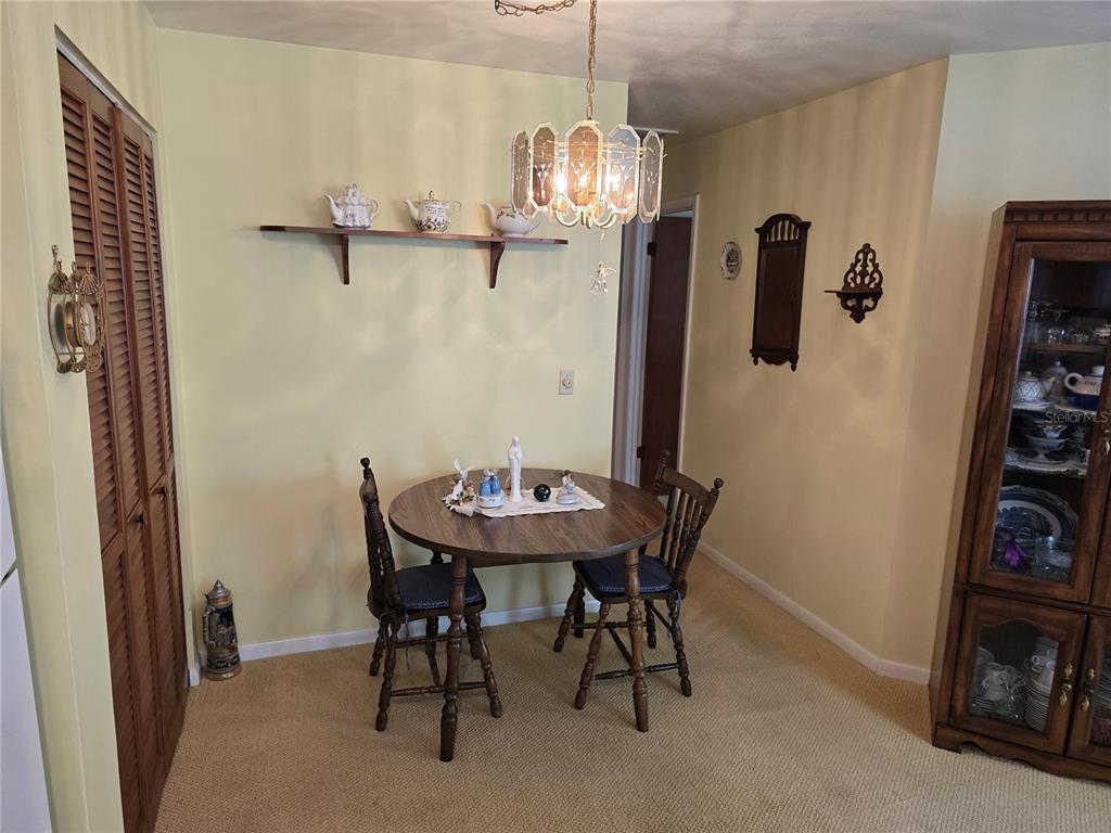 A dining area features a round wooden table, two chairs, a wall shelf, and chandelier — 4632 BLOSSOM BOULEVARD UNIT 4632, ZEPHYRHILLS, FL