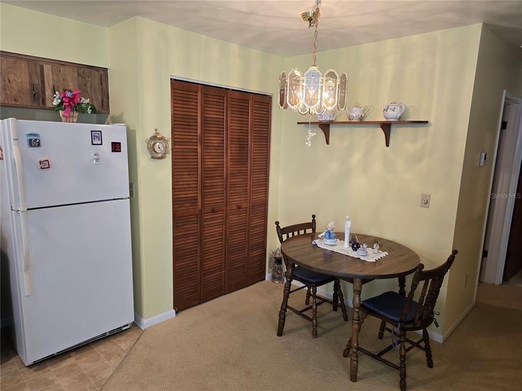 A dining area features a round wooden table, chairs, a chandelier, and a white refrigerator — 4632 BLOSSOM BOULEVARD UNIT 4632, ZEPHYRHILLS, FL