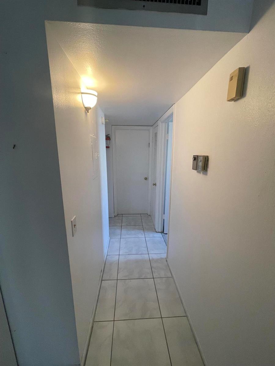 A narrow hallway with white walls, tiled flooring, and a door at the far end — 186 Flanders D # 186, Delray Beach FL 33484, DELRAY BEACH, FL
