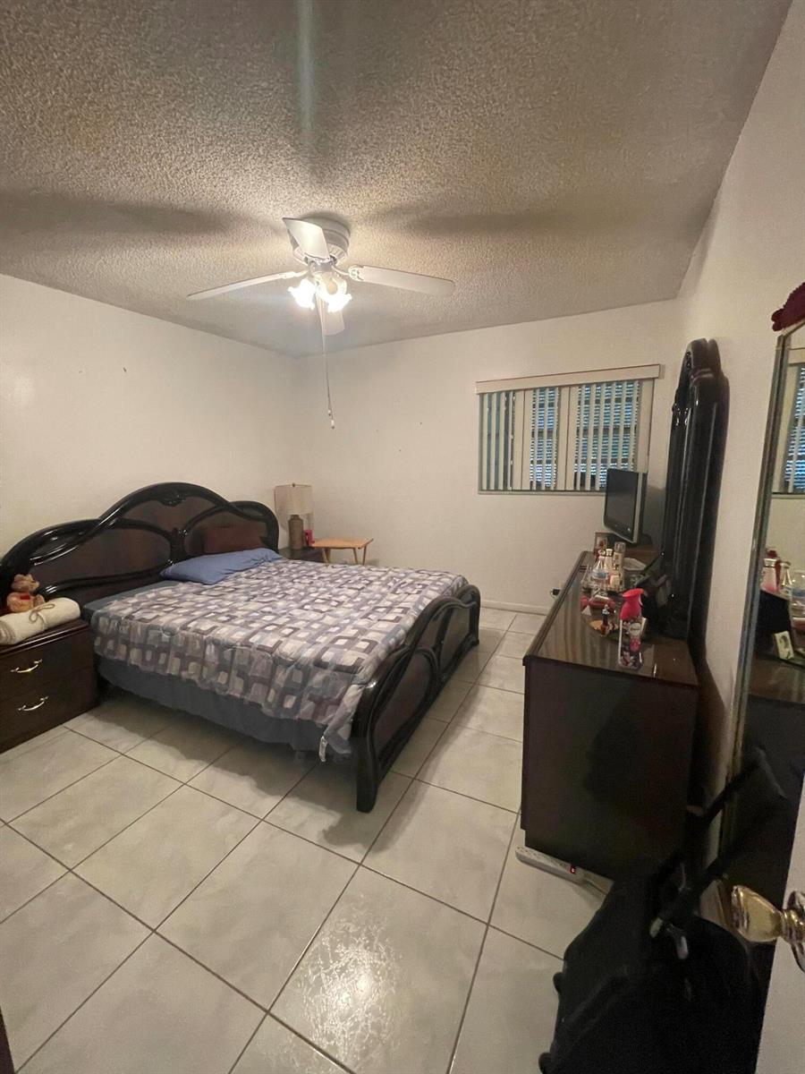 A bedroom features a dark wood bed frame, tile flooring, and a ceiling fan — 186 Flanders D # 186, Delray Beach FL 33484, DELRAY BEACH, FL
