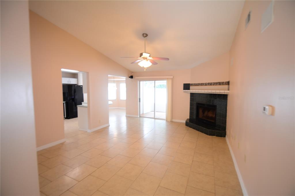 A living room with tile flooring, a vaulted ceiling, and a black tiled corner fireplace — 90 SLEEPY HOLLOW TRAIL, PALM COAST, FL