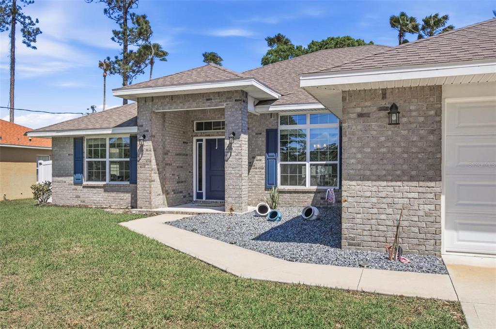 A single-story brick house with a blue front door, gray shutters, and a gravel garden — 80 BURNING BUSH DRIVE, PALM COAST, FL
