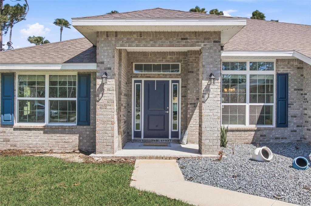 The front exterior of a brick house features a blue door, shutters, and a walkway — 80 BURNING BUSH DRIVE, PALM COAST, FL