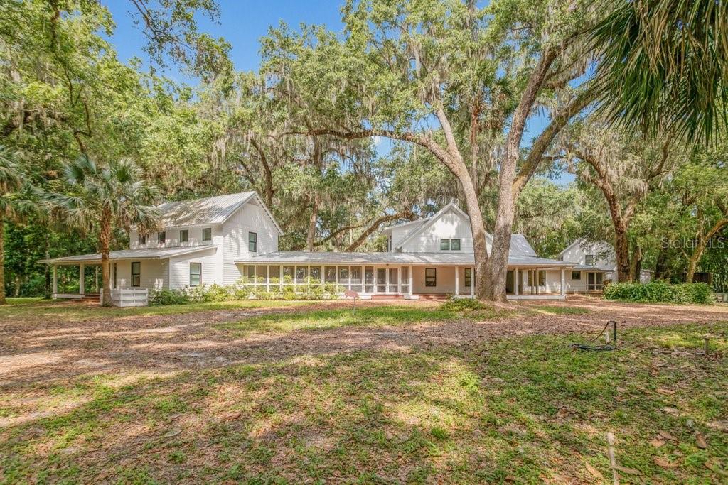 A white farmhouse with a metal roof and screened porch sits among large oak trees — 645 S US HIGHWAY 17, SAN MATEO, FL