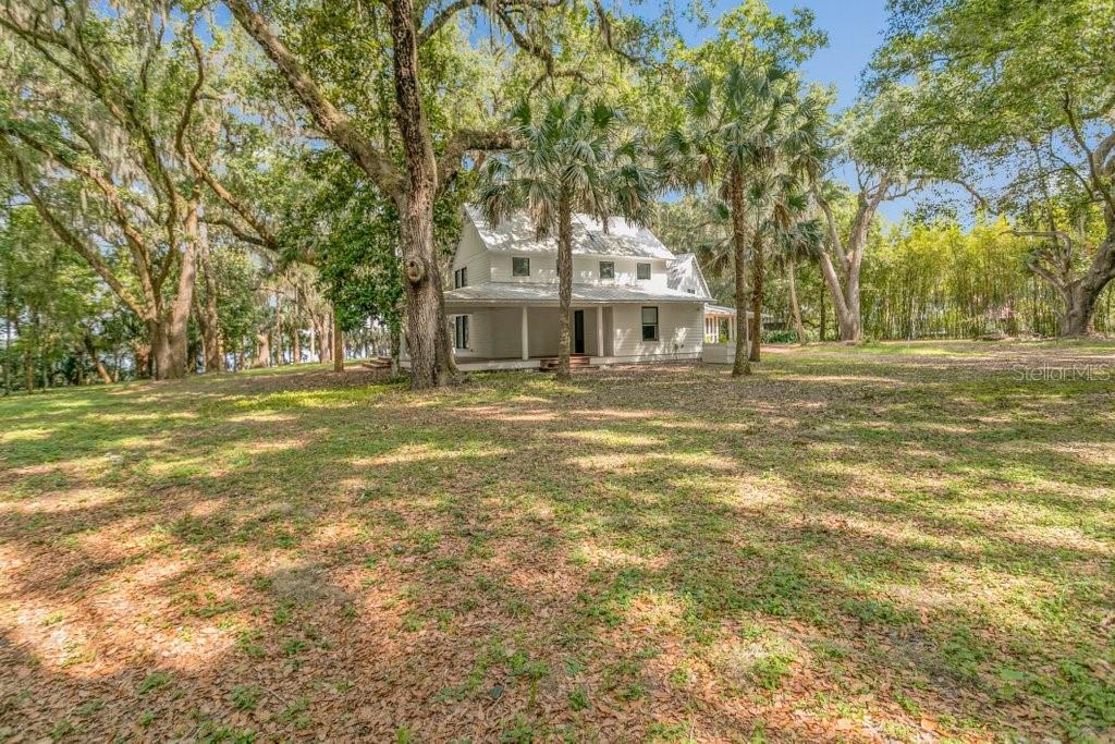 A white two-story farmhouse sits on a grassy lot surrounded by large trees — 645 S US HIGHWAY 17, SAN MATEO, FL