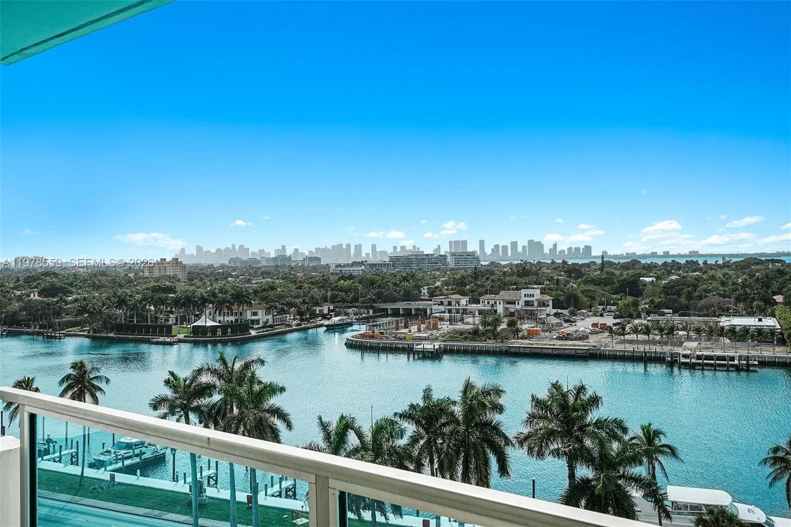 A balcony overlooks a canal, palm trees, and a distant city skyline under a clear sky — 5101 Collins Ave # 11T, Miami Beach FL 33140, MIAMI BEACH, FL