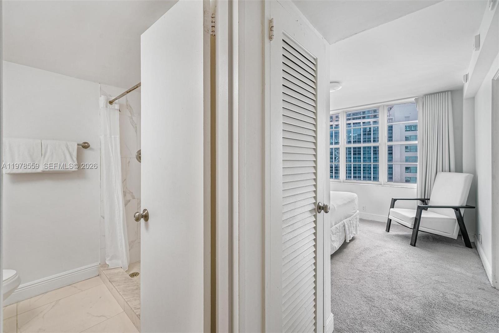 A view from a tiled bathroom into a carpeted bedroom with a white armchair — 5101 Collins Ave # 11T, Miami Beach FL 33140, MIAMI BEACH, FL