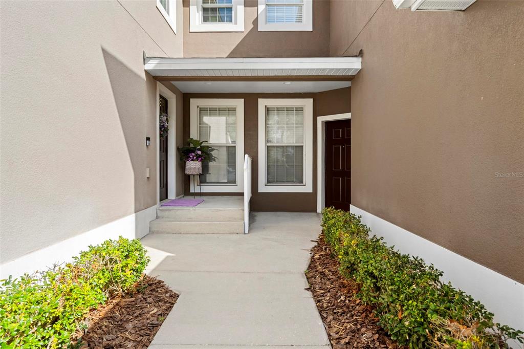 The exterior entrance of a multi-story home features a concrete walkway and two dark doors — 2105 KINGS PALACE DRIVE UNIT 2105, RIVERVIEW, FL