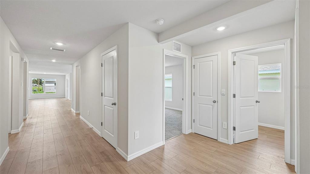 A hallway with light wood-look flooring leads to several rooms with white doors and walls — 17516 WHISKEY CREEK TRAIL, PARRISH, FL
