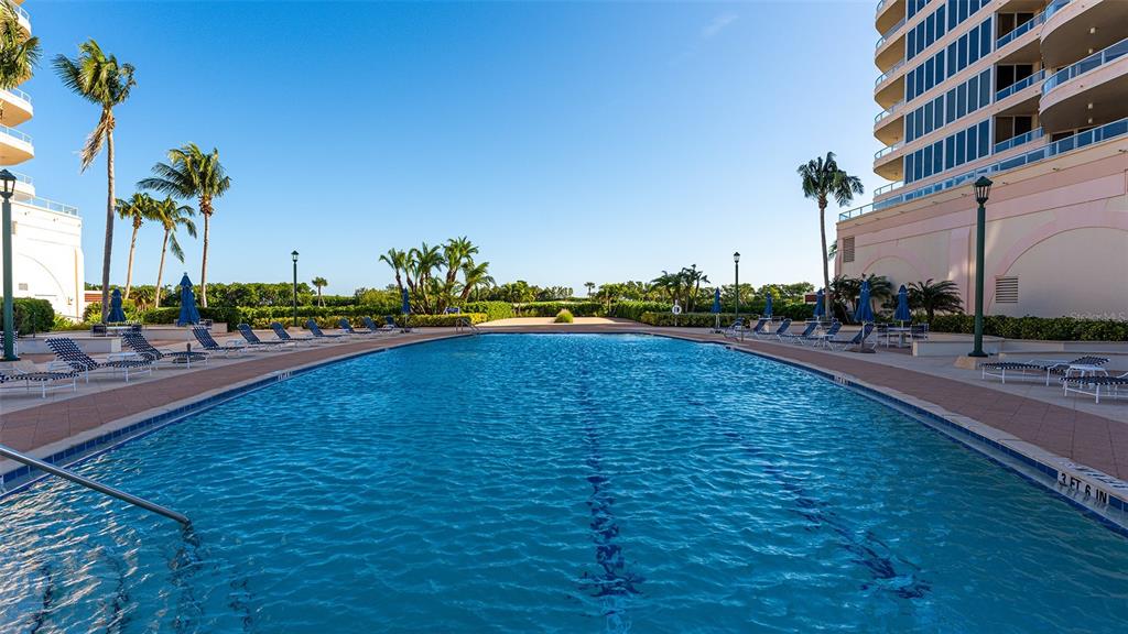 A large outdoor swimming pool is surrounded by lounge chairs, palm trees, and tall buildings — 3060 GRAND BAY BOULEVARD UNIT 172, LONGBOAT KEY, FL