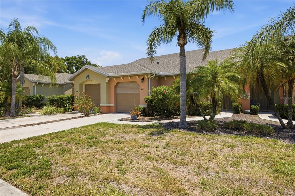 A single-story duplex with tan stucco walls, two garage doors, and several palm trees — 4620 1ST AVENUE E UNIT 4620, PALMETTO, FL