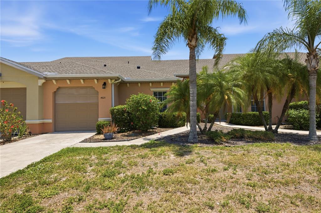 The exterior of a single-story house features a tan stucco facade, a garage, and palm trees — 4620 1ST AVENUE E UNIT 4620, PALMETTO, FL