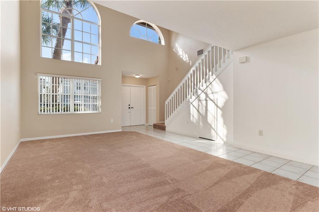 A living room with beige carpet, a white staircase, and a large arched window — 7697 NW 25th Street, Margate FL 33063, MARGATE, FL