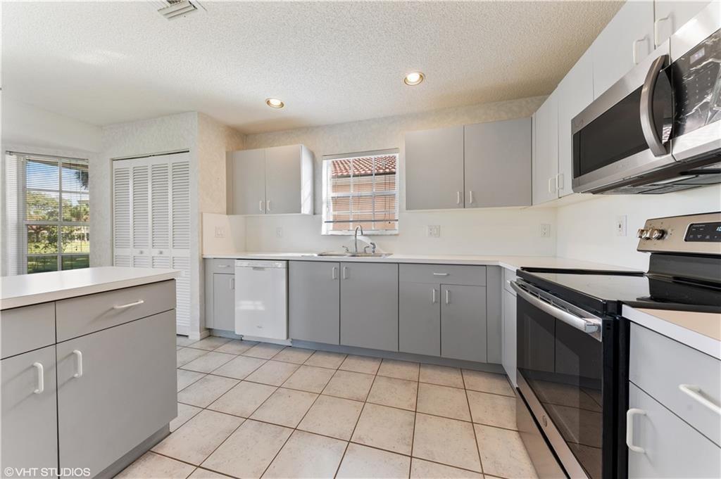 A kitchen features gray cabinets, white countertops, stainless steel appliances, and tile flooring — 7697 NW 25th Street, Margate FL 33063, MARGATE, FL