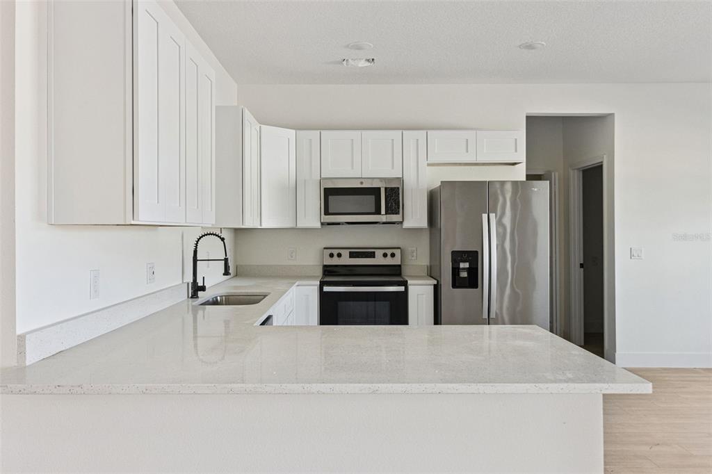 A modern kitchen features white cabinets, stainless steel appliances, and light-colored quartz countertops — 1201 APOPKA LANE, KISSIMMEE, FL
